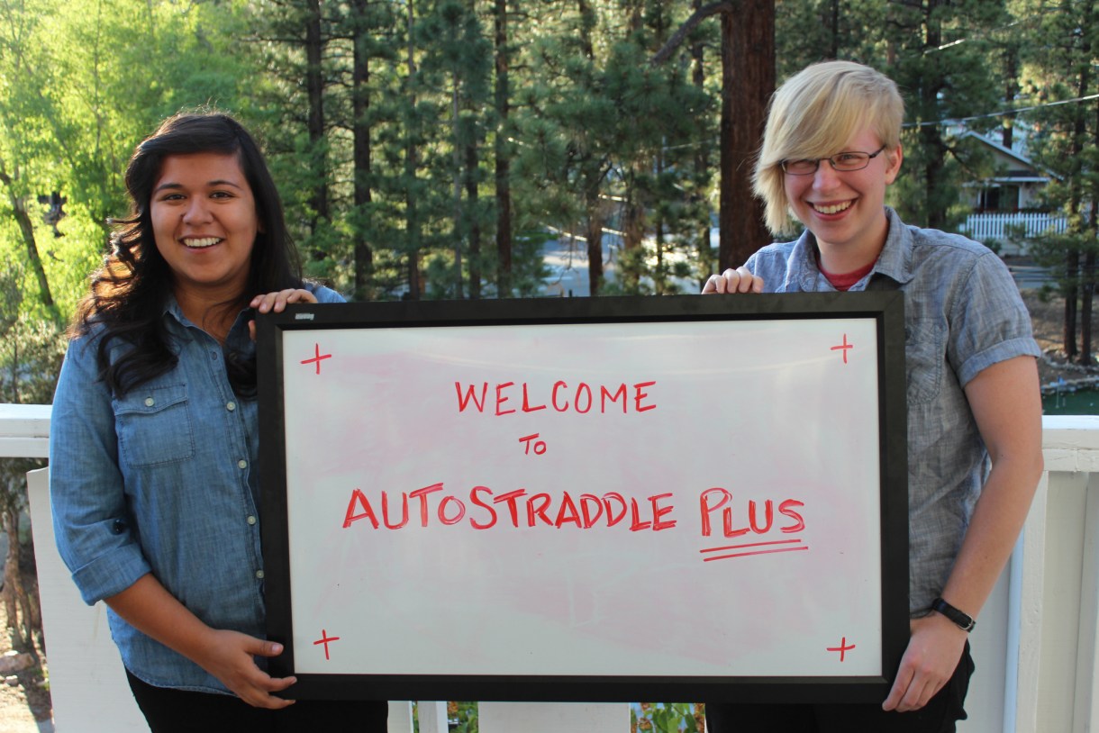 Yvonne and Grace holding a white board that says "Welcome to Autostraddle Plus"