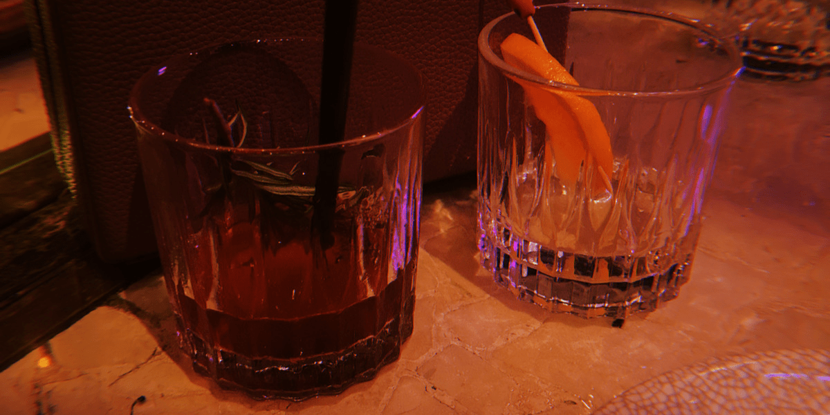 Two drink glasses in front of a purse