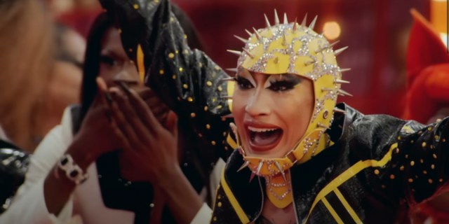 A still from Drag Race 1501 showing a contestant in a spikey headpiece and leather jacket