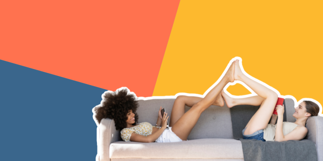 Two women on a couch reading have their feet in the air touching