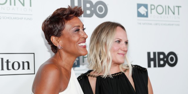 Robin Roberts and Amber Laign, now engaged, are together on a red carpet smiling to the right of camera.