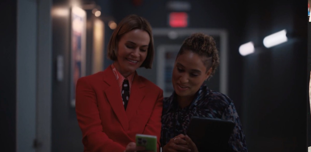 Alice pointing at a photo on her phone she's showing to Sophie