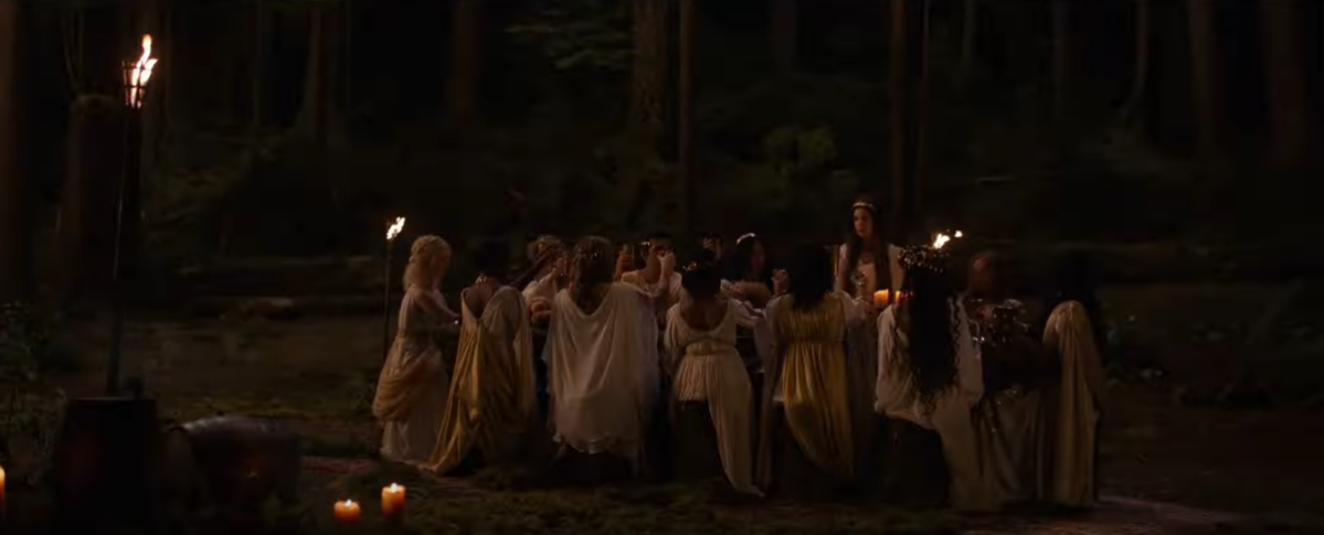 The Yellowjackets characters around a table in the woods wearing white and gold Ancient Greek looking gowns