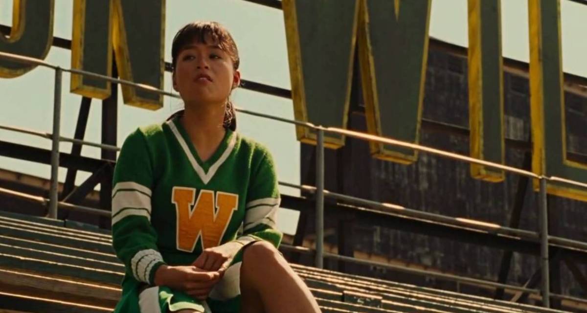 Prudence from Across the Universe (2007) sits on the bleachers wearing a green uniform