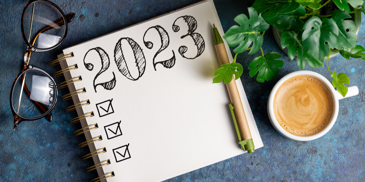 A journal that reads 2023 with check boxes on it. There are a pair of glasses and a coffee mug next to it.