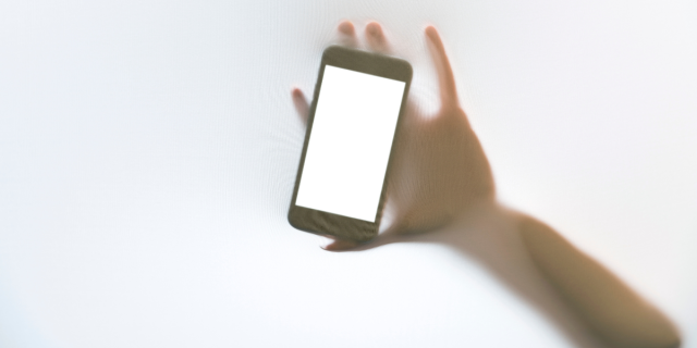 A hand holds a phone up against a blurry screen