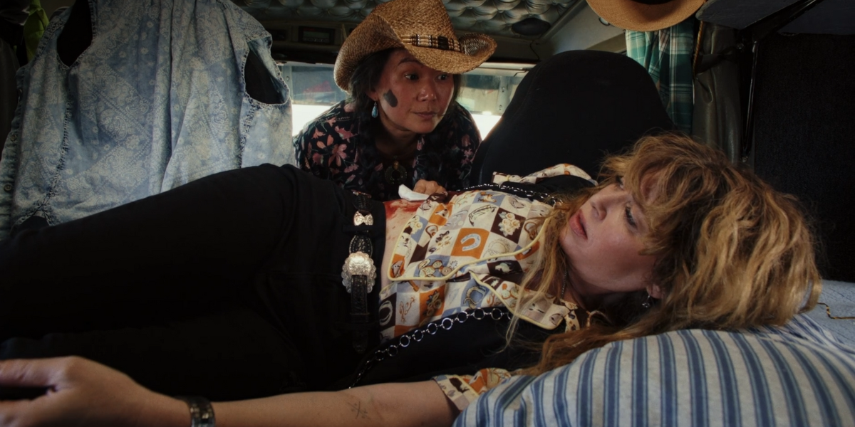 Hong Chau in Poker Face wears a cowboy hat and looks at Natasha Lyonne in a truck bed.