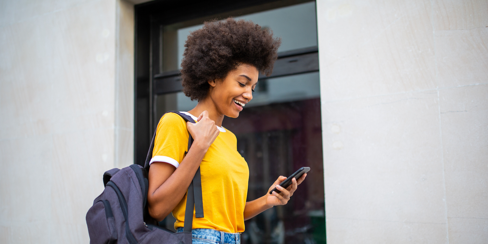 Side portrait of young Black woman walking with mobile phone and bag