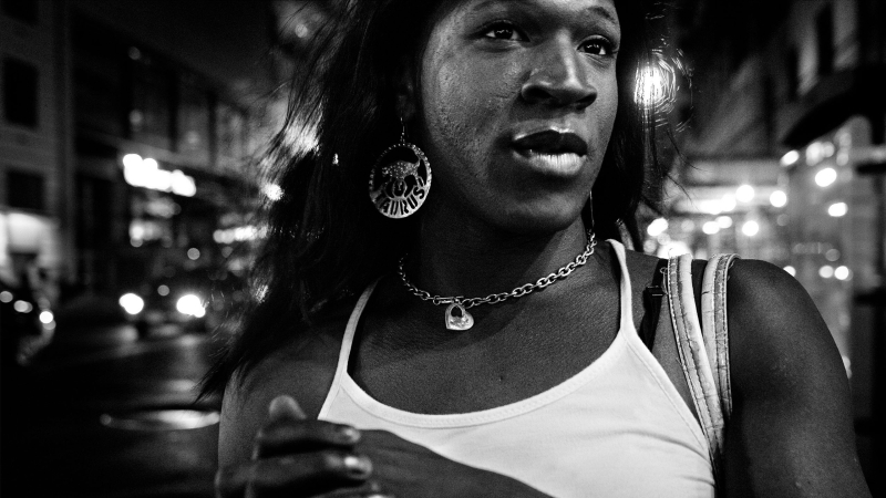 A black and white image of Kristen Parker Lovell in a white tank top and big earrings that say Taurus. 