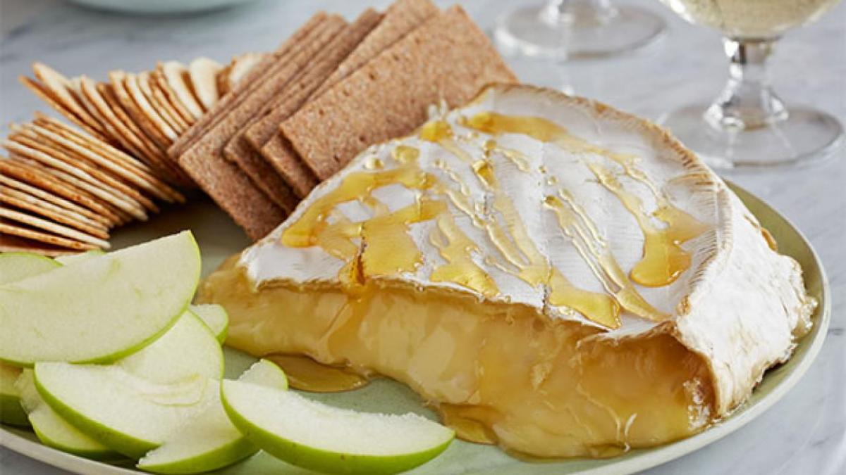 baked brie drizzled with honey and accompanied by crackers and sliced apples
