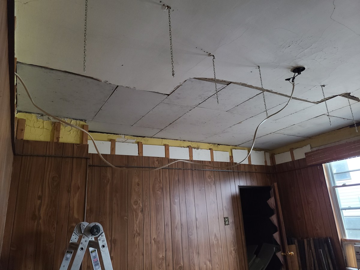 a photo of a ceiling that has been repaired extensively with drywall. there are still chains hanging from it that had previously been used to secure a drop ceiling.