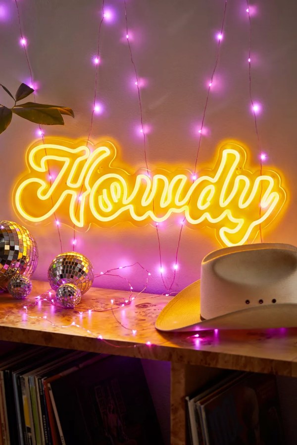 A yellow glowing sign of HOWDY in bubbly letters, next to a cowboy hat