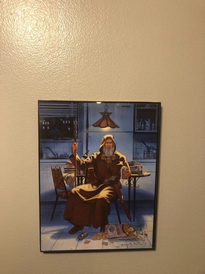 a photo of a piece of wizard art on my sister's wall that depicts a wizard in a brown robe with long white beard sitting in a city apartment kitchen holding a beer with chips spilled at the bottom of his feet