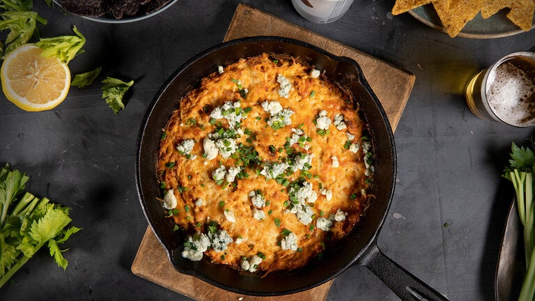 A small cast iron pan filled with cheese, chicken, buffalo sauce, and scallions