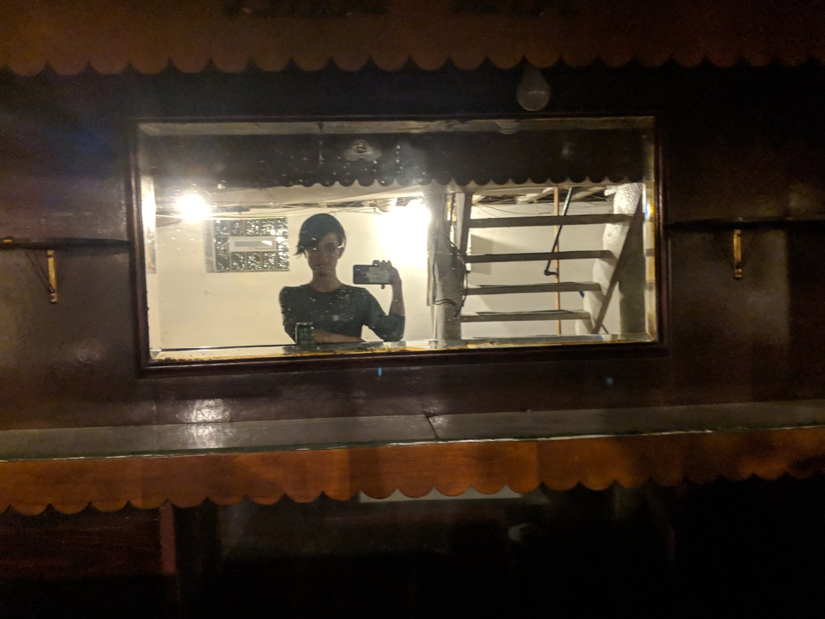 Nico takes a mirror selfie at the bar in their basement. it is a very old and dingy setup.