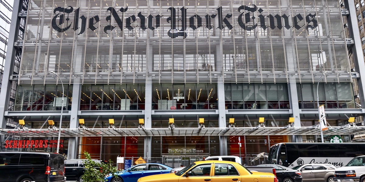 A taxi whizzes by in front of The New York Times building, the logo of which is front and center on the building's front