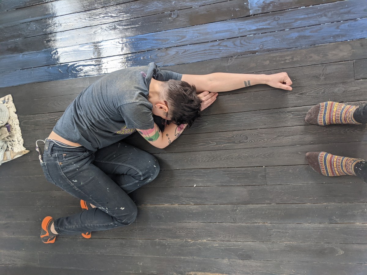 a photo of sadie in work clothes, lying on a half-finished floor, curled up in a ball, exhausted