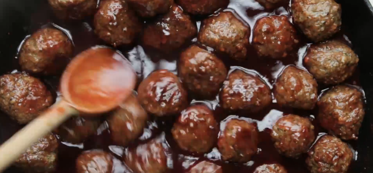 a pot of sauced meatballs with a wooden spoon