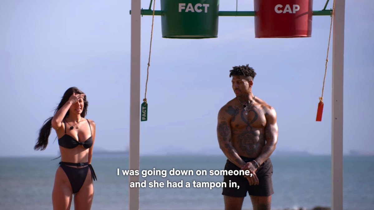 Still from Perfect Match: Francesca Farago in a green bikini standing on the beach next to Dom, who is underneath the two water buckets, dry. The caption reads: "I was going down on someone and she had a tampon in"