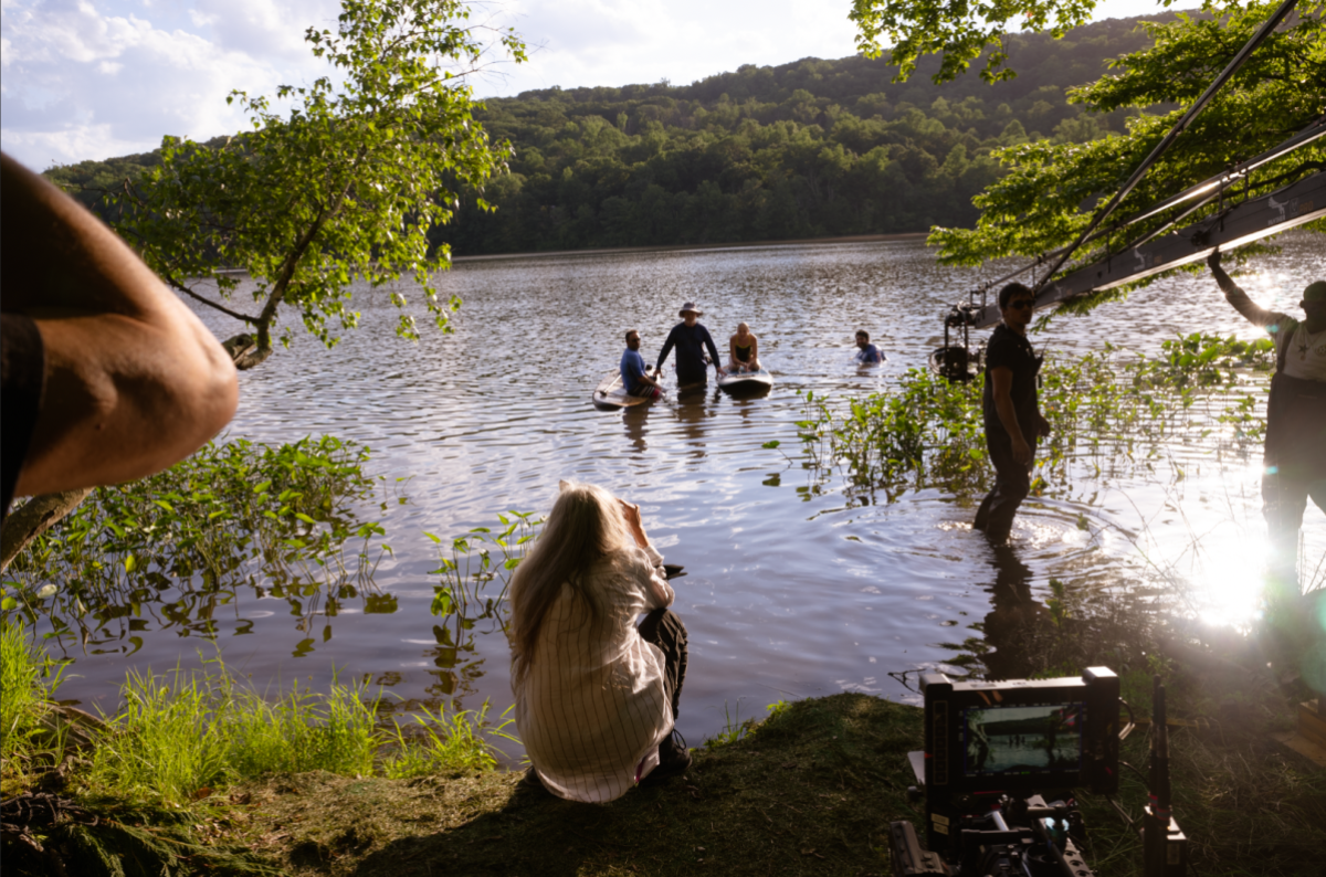 Annette Haywood-Carter crouches by a river at sunset looking toward her actors on boats.