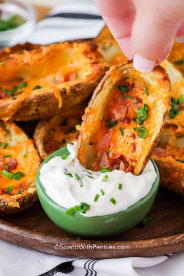 a hand dipping a loaded potato skin into a white sour cream based dip