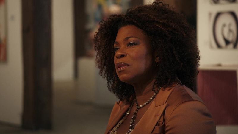 The Equalizer: Lorraine Toussaint's Aunt Vi sits on a bench (not pictured) at the art gallery and takes in the work of a young artist (also, not pictured). She's wearing a brown blazer and two necklaces.