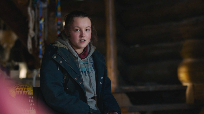 Ellie, wearing a sweatshirt and coat over her iconic red shirt, looks unimpressed.