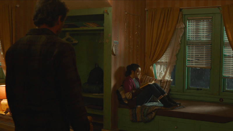 The Last of Us: We see the back of Joel as he stands to the side of the frame, looking at Ellie who is sitting on a window seat reading a teen girl's diary.