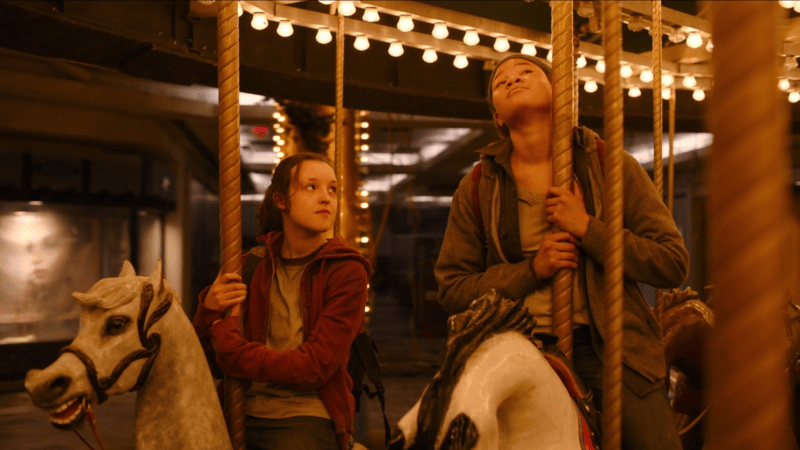 The Last of Us: Ellie and Riley are on a mall carousel, Ellie is looking wistfully up at Riley, who looks lost in thought.