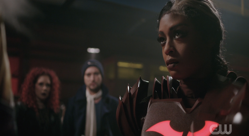 A screenshot of Ryan Wilder as Red Death on the Flash. Ryan is in the foreground and has a gray streak in her hair and is wearing a red batsuit with a broken bat logo. There are two rogues in the background.