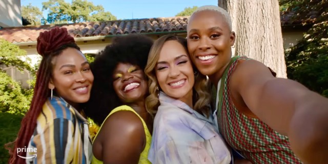 In a screenshot from the tv show Harlem, four Black women who are best friends squish their faces and shoulders together closely for a group selfie on a sunny day