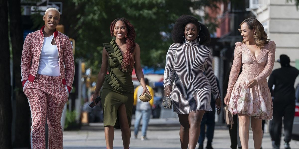 A group of four Black women from the TV show Harlem walk down the street in spring clothes on a sunny day in the famous Sex and the City walking formation.