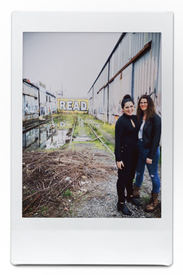 Kayla and Kristen stand in front of a graffiti wall in New Orleans that says READ
