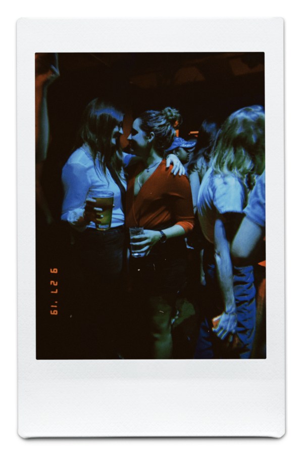 Kristen and Kayla in a crowded karaoke bar, looking at each other and holding beers