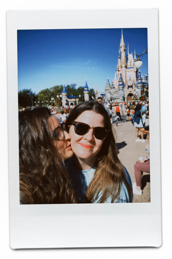 Kayla kisses Kristen's cheek in front of the castle at Disney World