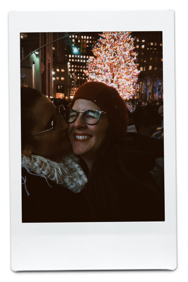 Kayla kisses Kristen's cheek in front of the NYC christmas tree
