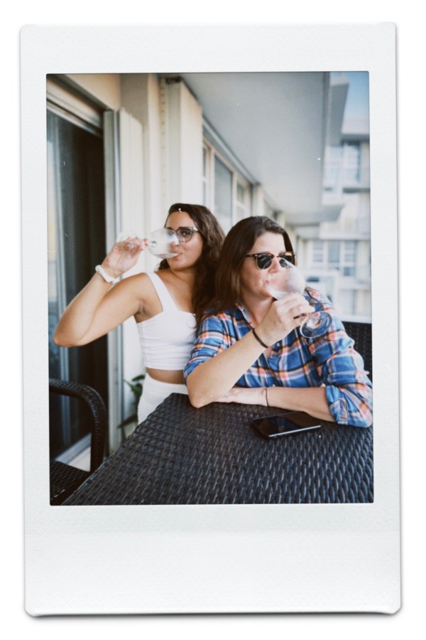 Kayla and Kristen hold large wine glasses and drink on their balcony in Miami