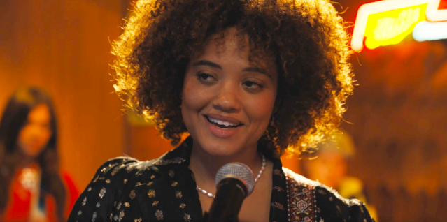 screenshot of kiersey clemons as cassidy in the movie somebody i used to know. she's standing up to a microphone on stage while smiling