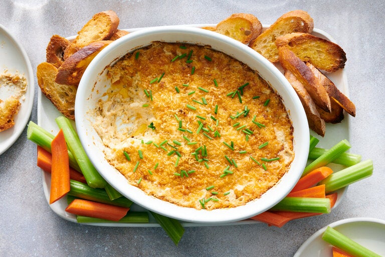 a casserole dish of spicy crab dip surrounded by crudites and toasts
