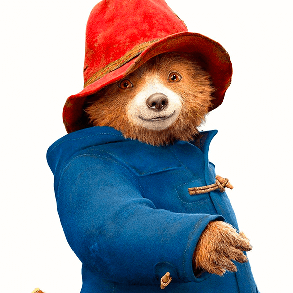 Paddington in his trademark blue pea coat and red hat. He's smiling. 