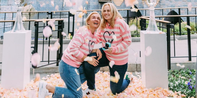 Rebel Wilson Engaged? Yes, indeed, she proposed to her girlfriend Ramona Agruma at Disneyland this weekend. In this photo, they're smiling in a bed of rose petals while wearing matching pink sweaters.