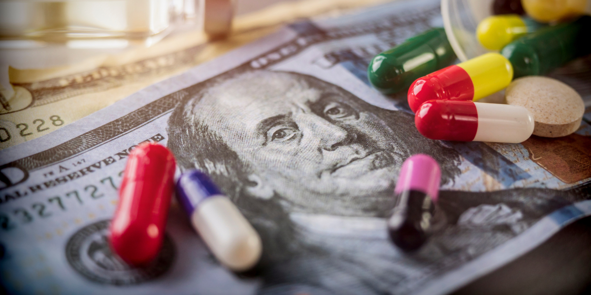 A bunch of pills on top of a bunch of cash, representing Big Pharma's profit greed