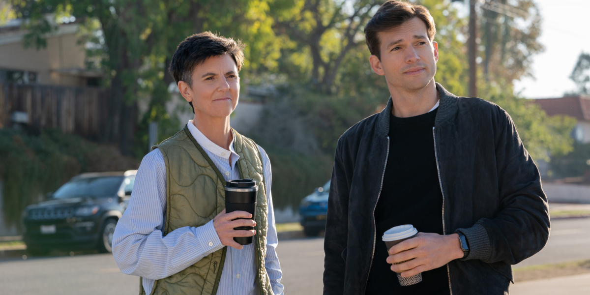 A still from Your Place or Mine: Tig Notaro in a green vest and blue buttondown holds a to-go coffee cup next to Ashton Kutcher in a black sweater and black bomber also holding a to-go coffee cup