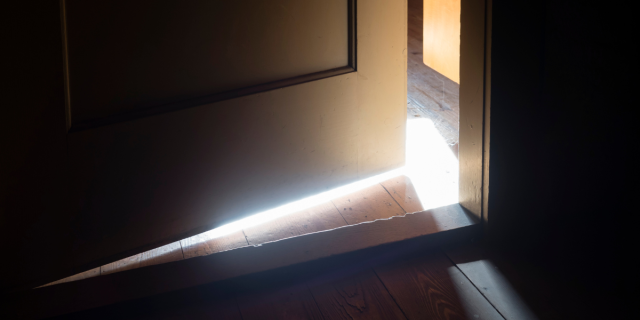a dark door is slightly ajar, letting out a leak of light