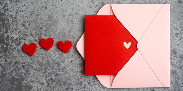 a red card with a white heart on it peeping out of a pink envelope. there are three felt red hearts next to it.