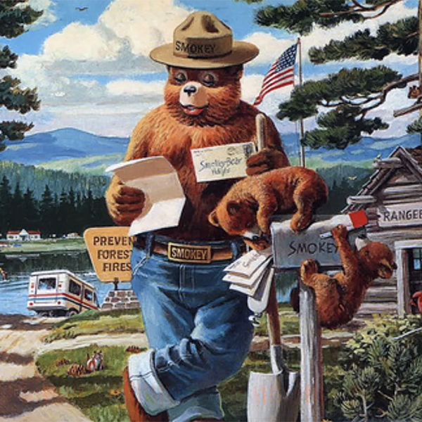 Smokey reads some letters by the mailbox while two bear cubs play on it. 