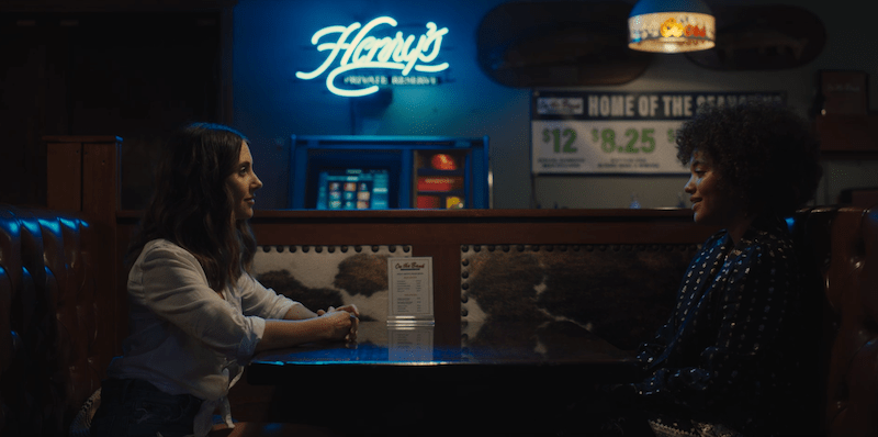 screenshot of alison brie and kiersey clemons sitting across the table from each other at a bar