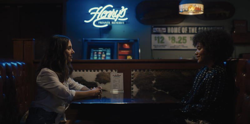 screenshot of alison brie and kiersey clemons sitting across the table from each other at a bar