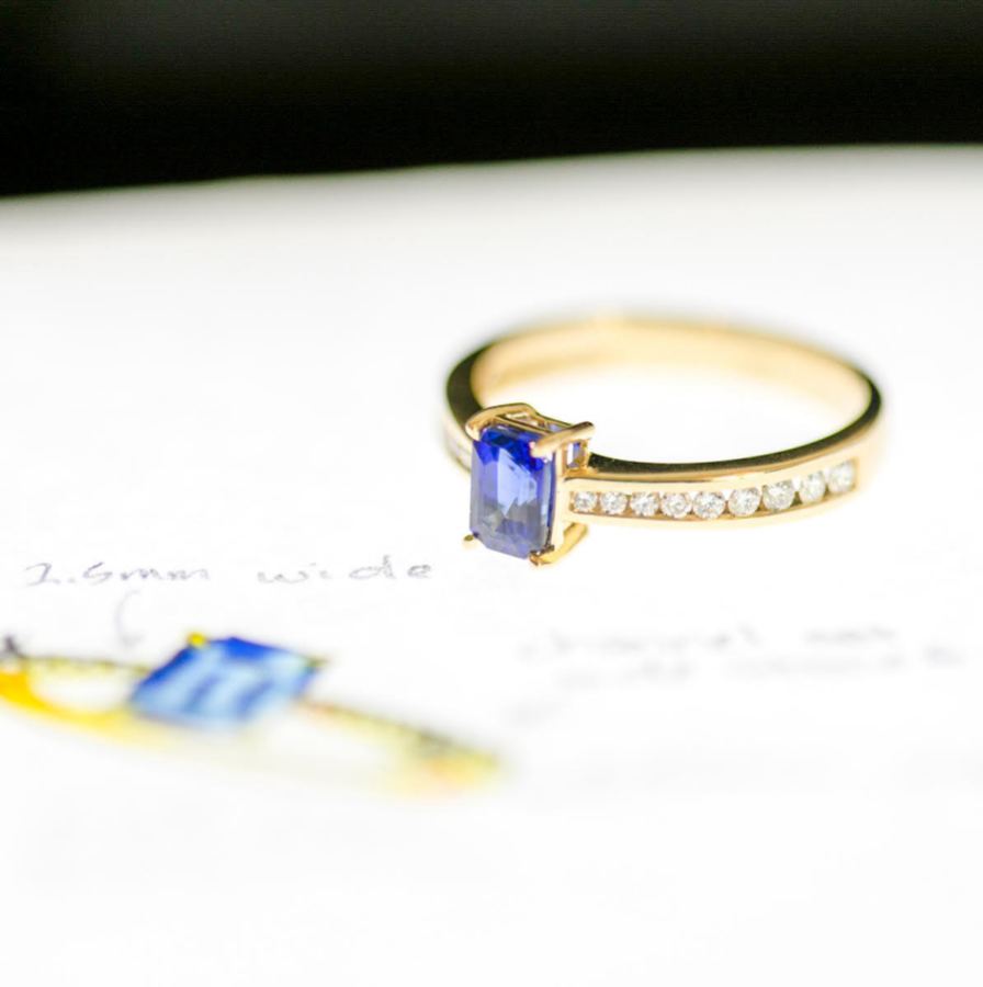 a gold ring with diamonds all around the band and a beautiful square cut blue stone in the center