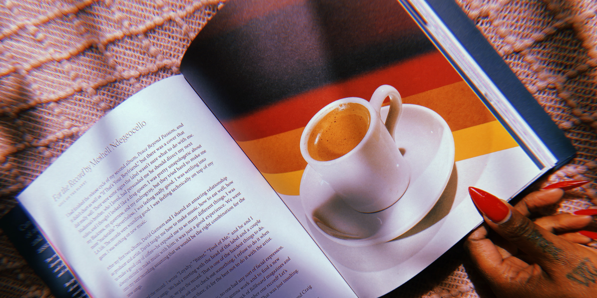 A photo of a perfect cup of coffee next to an essay inside of the book "Recipe for Disaster". A hand with painted pointy red nails holds the book open.
